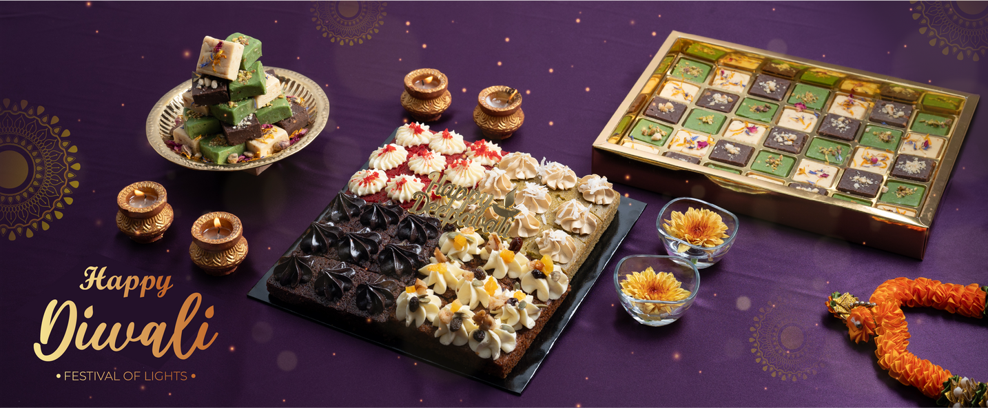 Diwali collection banner with a tray of assorted sweets and cake bites beside a marigold garland — Elevete Patisserie