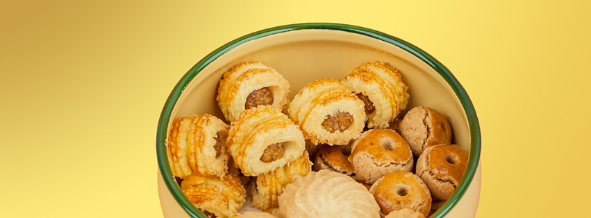 Open tin of pineapple tarts and assorted cookies on a yellow background — Elevete Patisserie