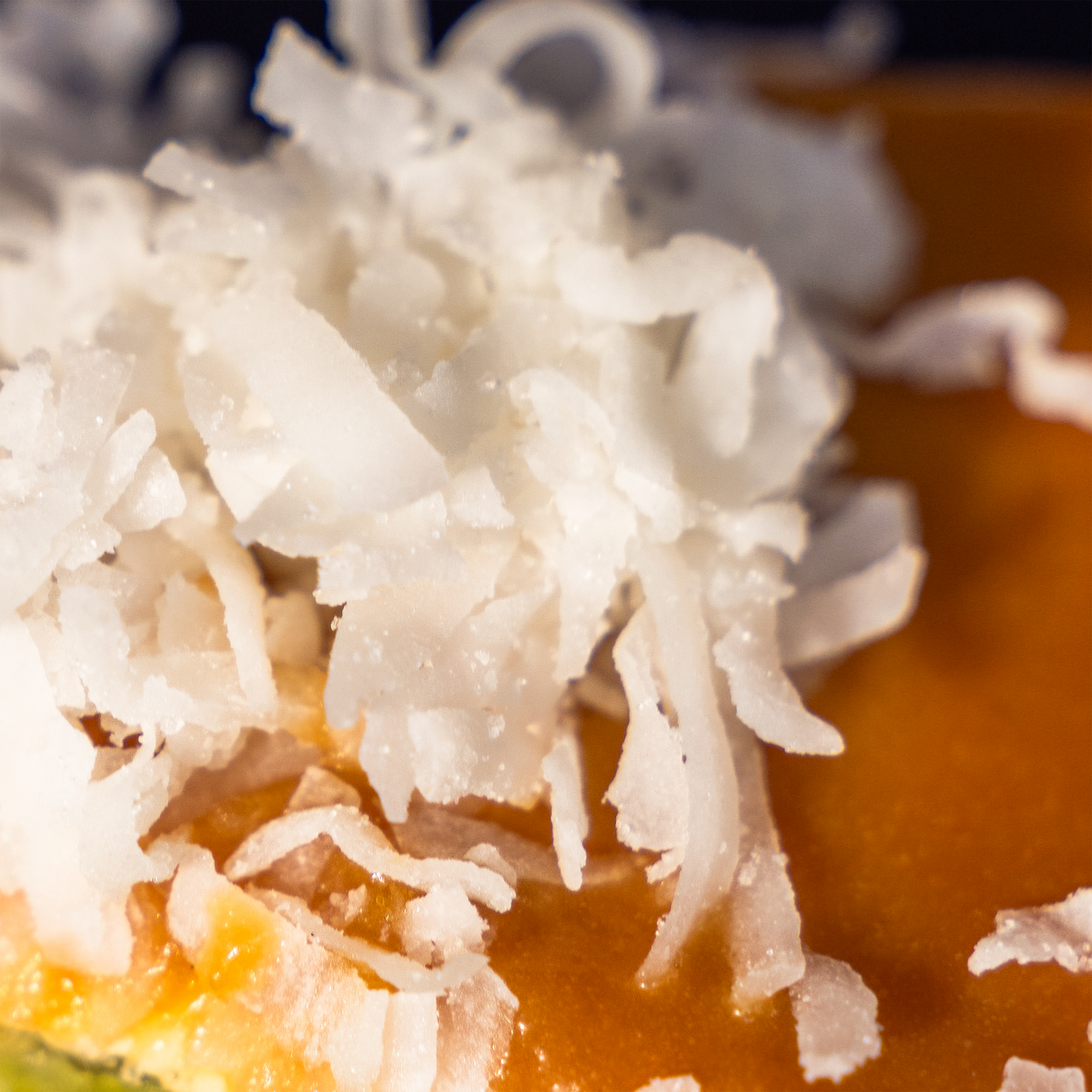 Macro detail of fresh shredded coconut scattered over glossy gula melaka glaze — Elevete Patisserie