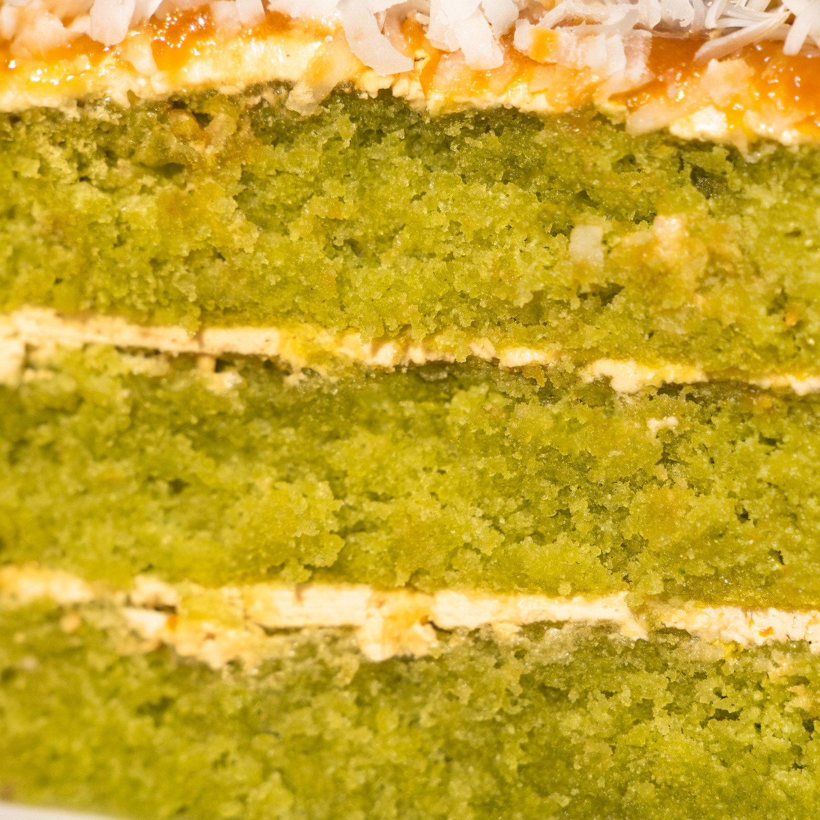 Close-up of layered pandan sponge and pale buttercream under a gula melaka glaze and shredded coconut — Elevete Patisserie