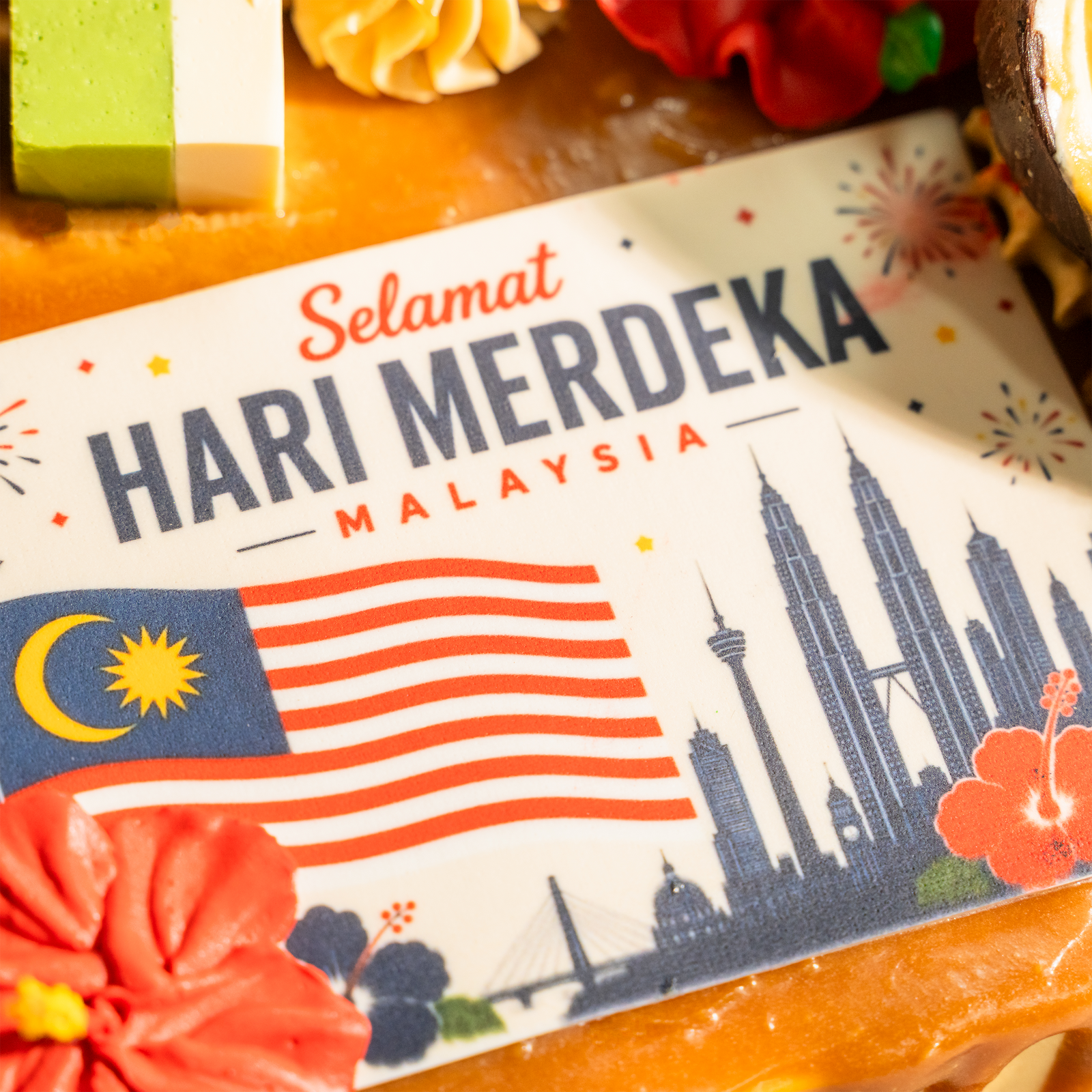 Close-up of the Selamat Hari Merdeka plaque on the Muhibbah cake — Malaysian flag, Kuala Lumpur skyline and a red hibiscus
