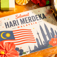 Close-up of the Selamat Hari Merdeka plaque on the Muhibbah cake — Malaysian flag, Kuala Lumpur skyline and a red hibiscus