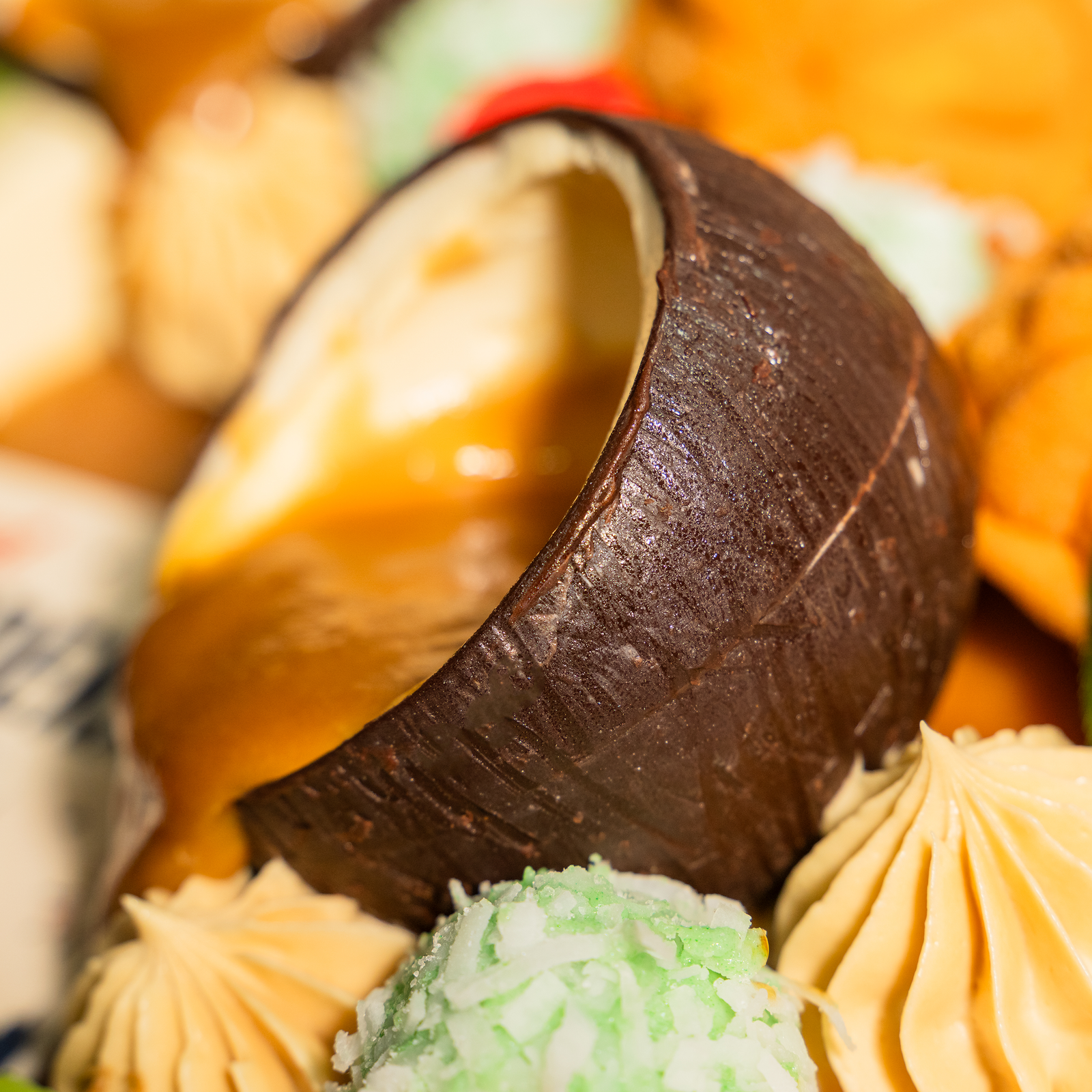 Close-up of a coconut shell filled with warm gula melaka sauce on the Muhibbah kuih cake