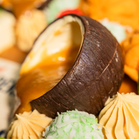 Close-up of a coconut shell filled with warm gula melaka sauce on the Muhibbah kuih cake