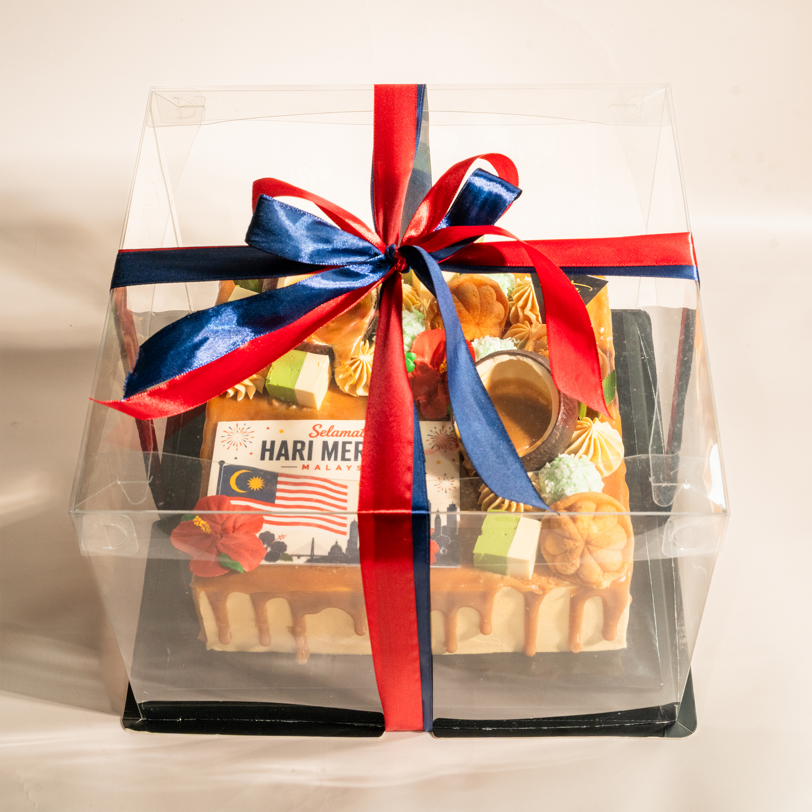 Muhibbah Merdeka kuih cake boxed as a gift in a clear case with red and blue ribbon